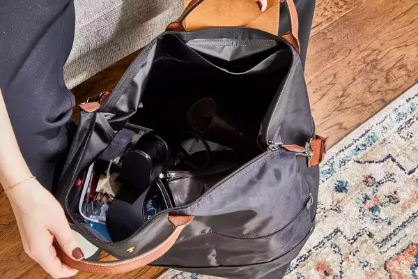 A hand opening the Longchamp Le Pliage Expandable Travel Bag filled with items