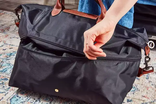 A person opening the zipper to the Longchamp Le Pliage Expandable Travel Bag