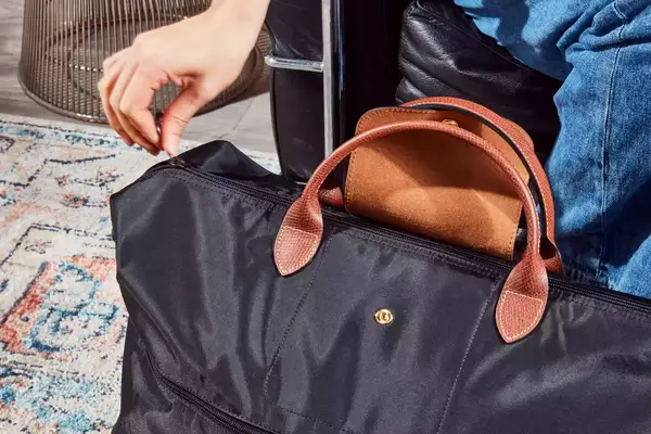 A person zipping the Longchamp Le Pliage Expandable Travel Bag