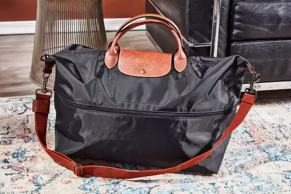 The Longchamp Le Pliage Expandable Travel Bag on a rug next to furniture