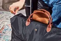 A person zipping the Longchamp Le Pliage Expandable Travel Bag