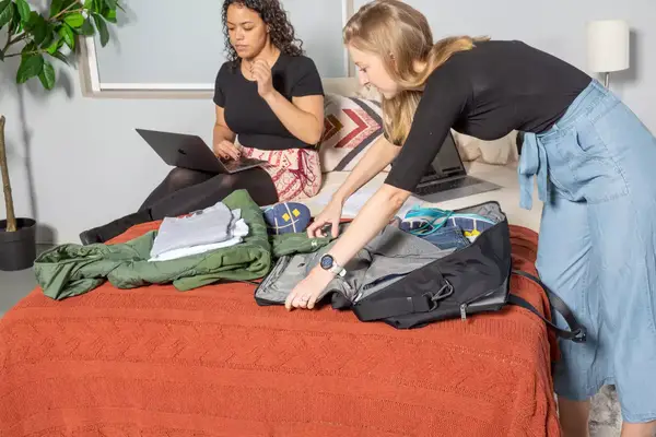 Person unpacking Away The Large Everywhere Bag with another person sitting on bed