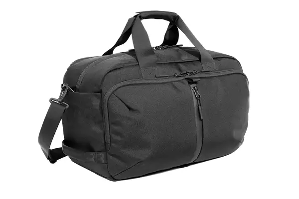 A hand packing a laptop into the Calpak Luka Duffel Bag