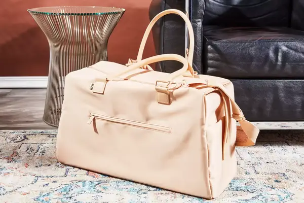 Béis The Commuter Duffle sitting on a rug in front of a couch 