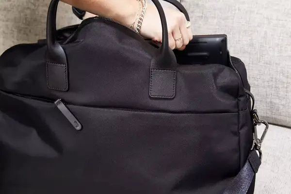 Person opening Away The Large Everywhere Bag on bed with another person sitting on bed nearby