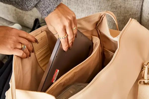 A person placing a laptop into the sleeve of the Béis The Commuter Duffle