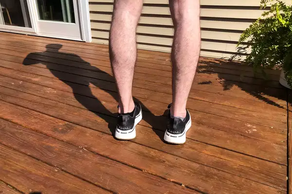 The back-view of a person wearing AHNU Sequence 1 sneakers on a wooden deck