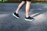 A person walking on blacktop while wearing AHNU Sequence 1 sneakers