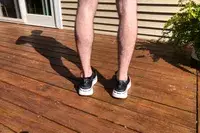 The back-view of a person wearing AHNU Sequence 1 sneakers on a wooden deck