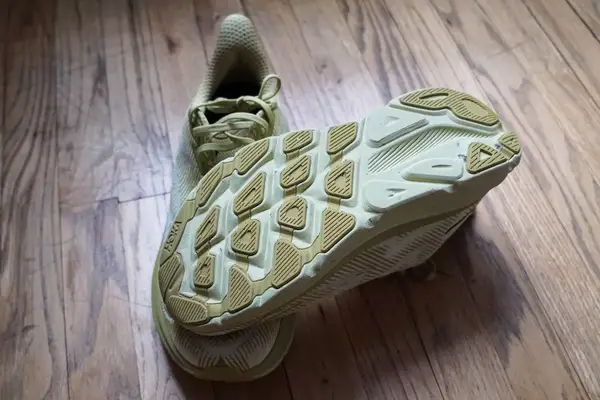 Two Hoka Clifton 9 sneakers posed on a wooden floor to show the bottom of the shoe