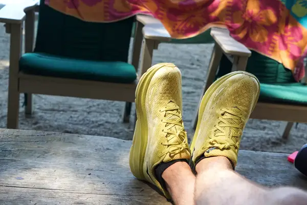 Two legs crossed on wood while wearing Hoka Clifton 9 sneakers