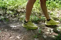 A close-up of two legs wearing Hoka Clifton 9 sneakers while walking in dirt