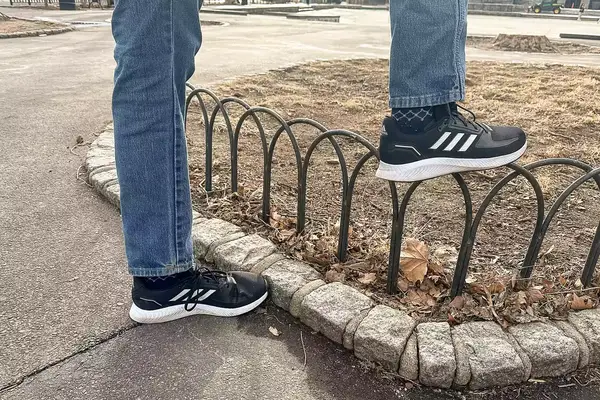 Person putting their feet on a fence wearing gray Adidas Men