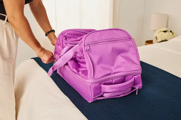 A person touching the Vera Bradley Adair Rolling Duffel Bag on a bed