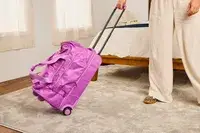 A person rolling the Vera Bradley Adair Rolling Duffel Bag on a rug