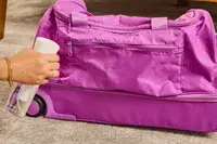 A person spraying the Vera Bradley Adair Rolling Duffel Bag with water