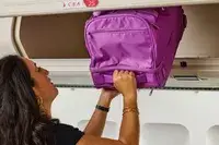 A person putting the Vera Bradley Adair Rolling Duffel Bag into an overhead bin