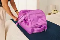 A person touching the Vera Bradley Adair Rolling Duffel Bag on a bed