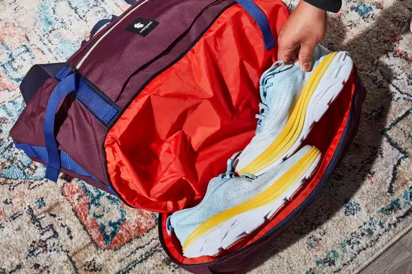 A hand putting a shoe into the Cotopaxi Viaje 35L Weekender Bag - Cada Día