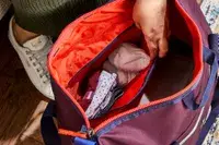 Hand reaching into a filled Cotopaxi Viaje 35L Weekender Bag - Cada Día