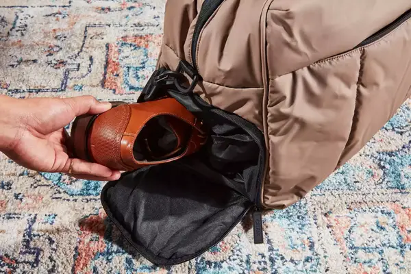 A hand packing a shoe inside the Calpak Luka Duffel Bag