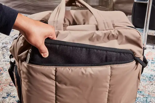 A hand packing a laptop into the Calpak Luka Duffel Bag
