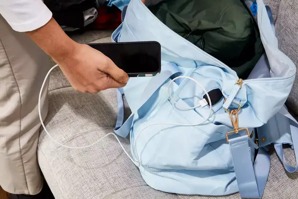 Hand holding a phone plugged into the ETRONIK Large Overnight Weekender 55L
