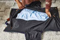 Hands zipping the Mark & Graham Commuter 2-in-1 Garment Bag with clothing inside