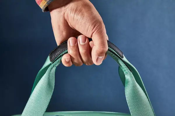 Close-up of a hand holding the Arlo Skye The Weekender top handles against a blue background
