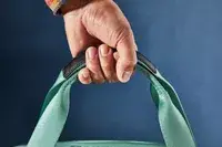 Close-up of a hand holding the Arlo Skye The Weekender top handles against a blue background
