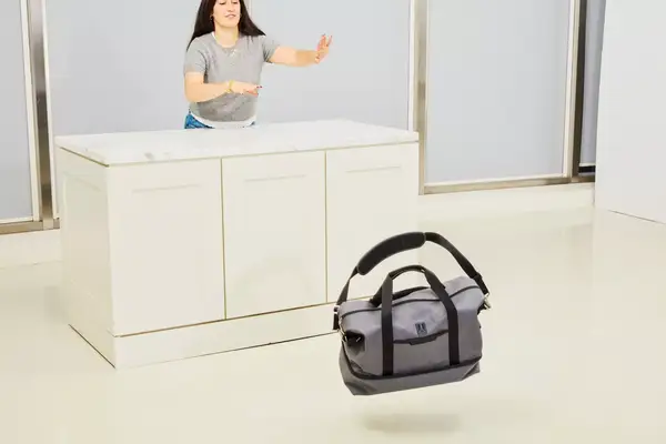 A person pushing the Travelpro x Travel & Lanetrek Drop-bottom Weekender Bag off of a counter