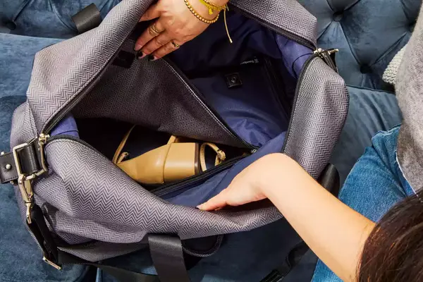 Hands opening the Travelpro x Travel & Lanetrek Drop-bottom Weekender Bag main compartment