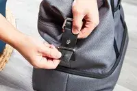 Hands snapping a closure on the Travelpro x Travel & Lanetrek Drop-bottom Weekender Bag