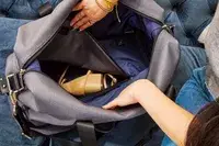 Hands opening the Travelpro x Travel & Lanetrek Drop-bottom Weekender Bag main compartment