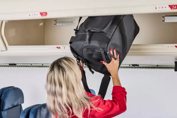 A person places the Rains Large Texel Kit Bag into an overhead compartment