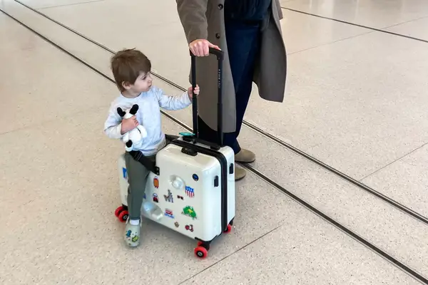 A child sitting on the Cegali Itsy Rider 20-inch Ride-on Suitcase for Kids with a person holding the handle