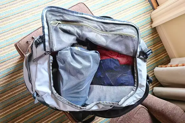 An open Cotopaxi Allpa Getaway 70L Duffel on a chair with clothing items visible inside