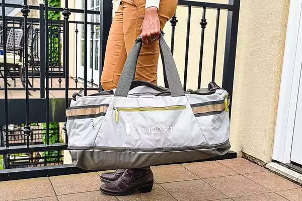 Person holding a Cotopaxi Allpa Getaway 70L Duffel, standing outside on a balcony