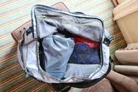 An open Cotopaxi Allpa Getaway 70L Duffel on a chair with clothing items visible inside