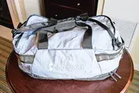 A Cotopaxi Allpa Getaway 70L Duffel with handles and zippers on a wooden table