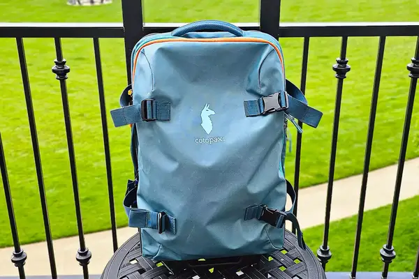 Cotopaxi Allpa 65L Roller Bag on an outdoor table, railing in background