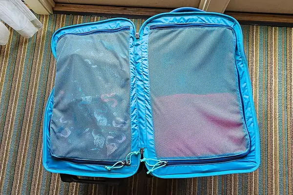 An open Cotopaxi Allpa 65L Roller Bag with clothing compartments visible, placed on a striped carpet floor