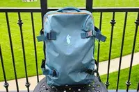 Cotopaxi Allpa 65L Roller Bag on an outdoor table, railing in background