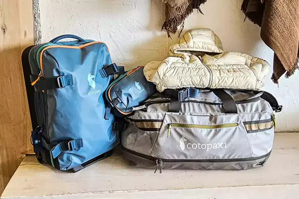 Two backpacks and a rolled jacket from the brand Cotopaxi placed on a wooden surface