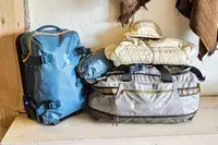 Two backpacks and a rolled jacket from the brand Cotopaxi placed on a wooden surface