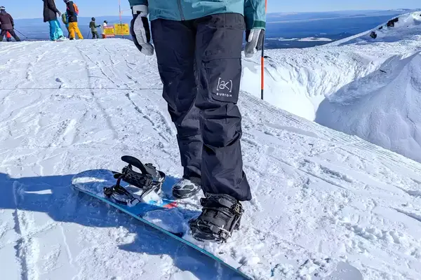 A close-up of a person stepping onto a snowboard while wearing the Burton Women’s AK Summit GORE-TEX 2L Pants