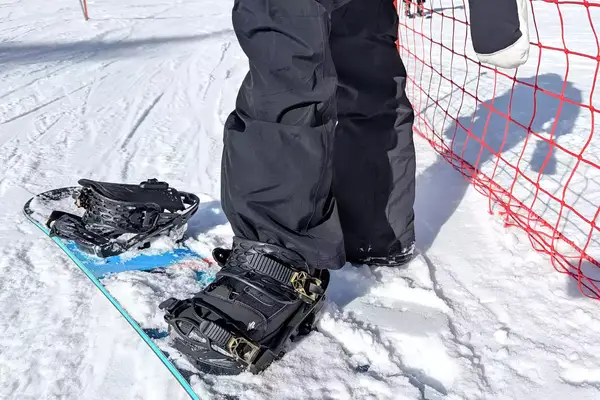 A close-up of a person stepping onto a snowboard while wearing the Burton Women’s AK Summit GORE-TEX 2L Pants