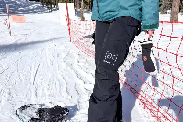 A person leaning on a red fabric fence while wearing the Burton Women’s AK Summit GORE-TEX 2L Pants