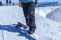 A close-up of a person stepping onto a snowboard while wearing the Burton Women’s AK Summit GORE-TEX 2L Pants