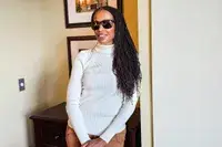 Person standing indoors wearing a white turtleneck sweater and Ray-Ban Chromance Sunglasses